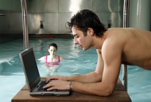Man on computer next to a swimming pool