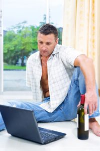Man with a bottle of wine sitting in front of a laptop