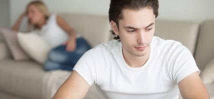 Troubled young handsome man, woman at the background on the sofa